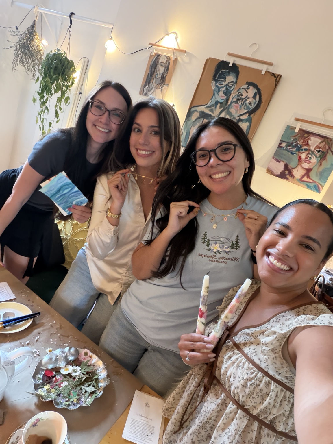 Four women smiling together and showing the necklaces and candles they created at a gathering